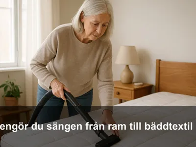 En person dammsuger madrassen längs sömmarna med ett borstmunstycke i ett ljust sovrum.