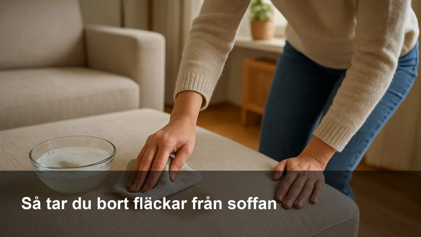 Hand som duttar bort en fläck på en ljus tygsoffa med mikrofiberduk och liten skål med såpvatten intill