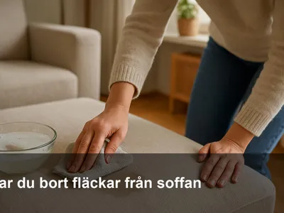 Hand som duttar bort en fläck på en ljus tygsoffa med mikrofiberduk och liten skål med såpvatten intill