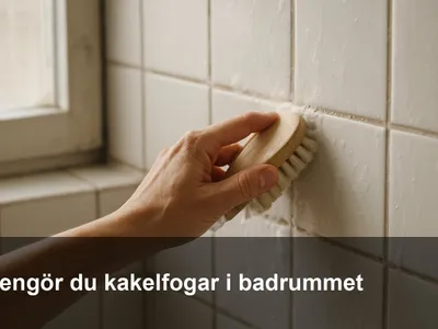 Närbild på hand som skrubbar kakelfog i duschen med en liten mjuk borste och lätt såplödder.