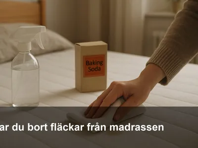 Hand som baddar en fläck på en vit madrass med en ren trasa, sprejflaska och bikarbonat bredvid.