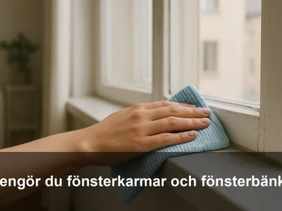 Hand som torkar en vit fönsterkarm och fönsterbänk med blå mikrofiberduk i dagsljus.
